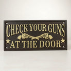 Jones Peak cast iron wall plaque with raised gold lettering reading "CHECK YOUR GUNS AT THE DOOR" and crossed revolvers.