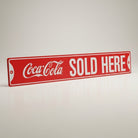 Jones Peak Coca-Cola Sold Here embossed red metal street sign with white lettering, 6" x 36".